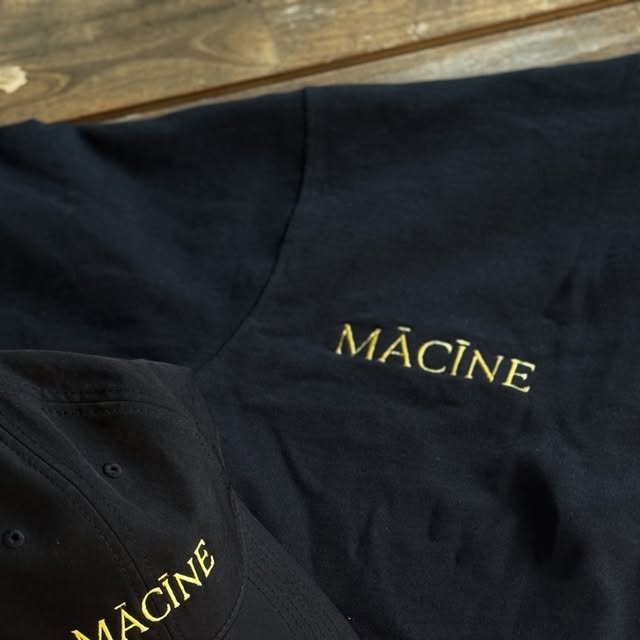 MĀCĪNE merch — black cap and tee with gold embroidered wordmark